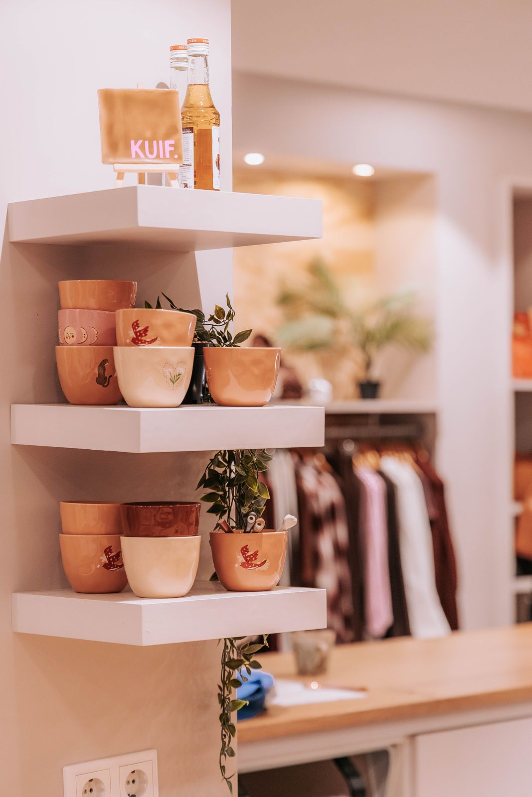 De bar: planken bij de bar van KUIF met aardewerk kopjes, planten en KUIF-flessen