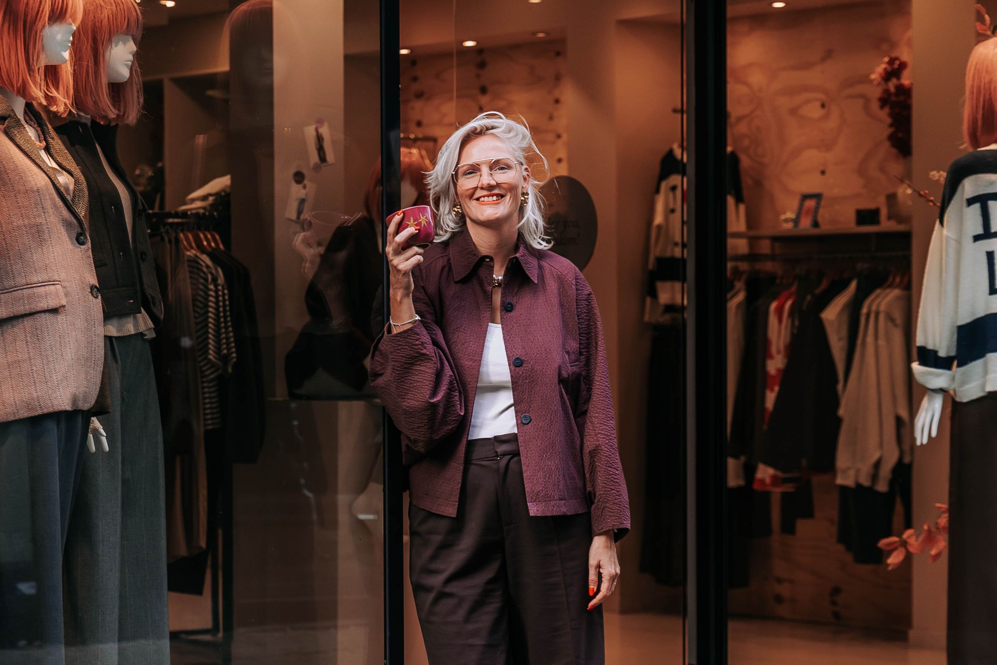 Ellie Thijssen lachend in de deur van KUIF aan de Klaasstraat, met een kop koffie