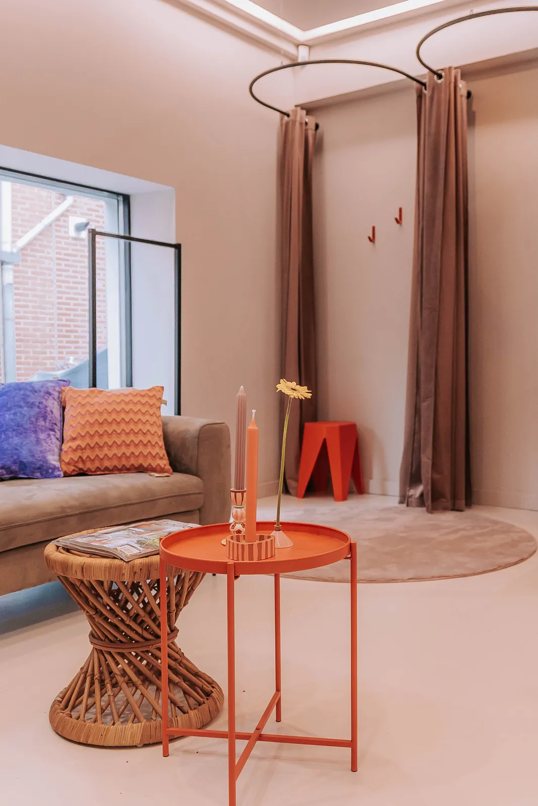 De zithoek in de huiskamer van KUIF: bank met kussens, een oranje bijzettafel en de paskamers met gordijnen