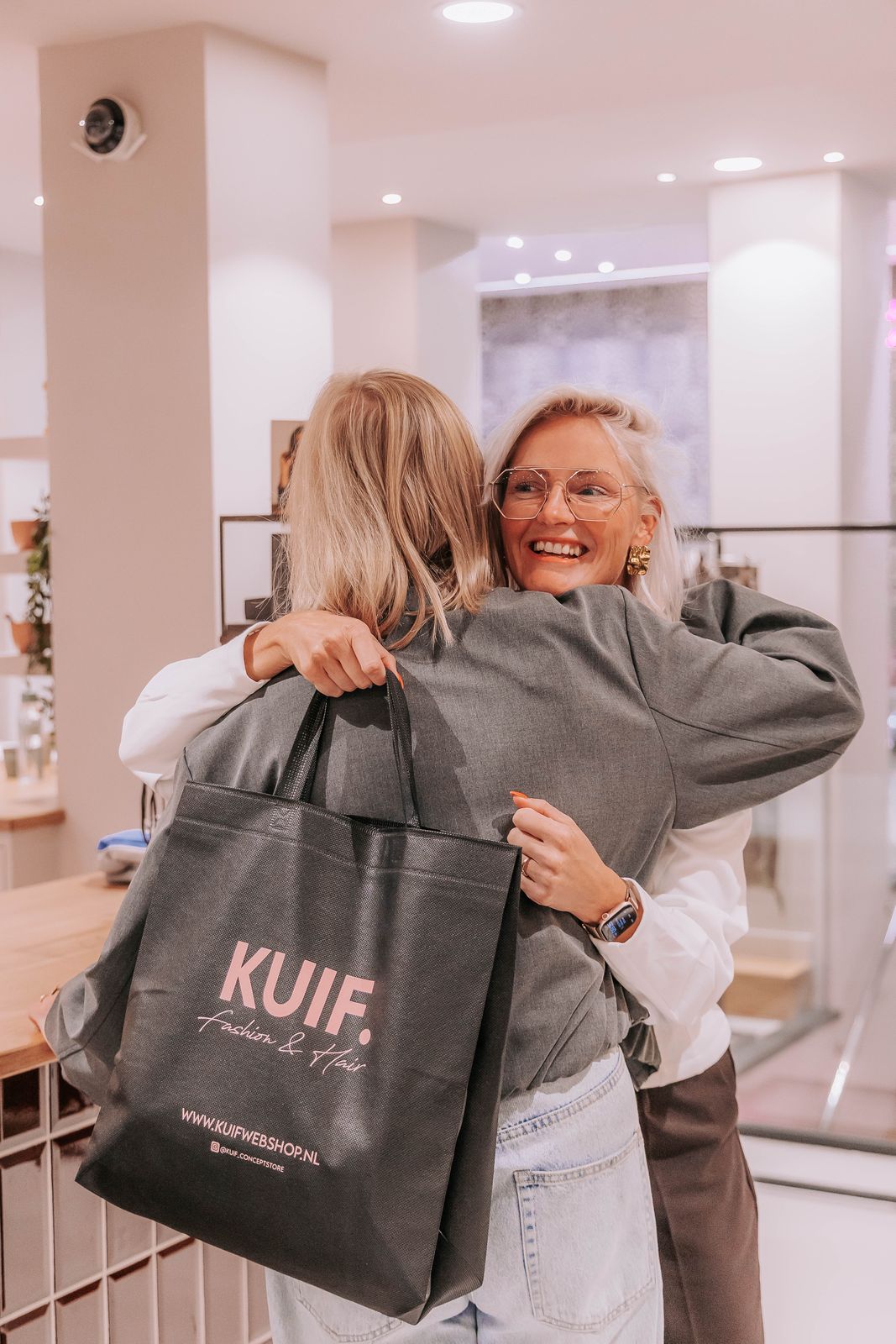 Ellie knuffelt een klant met een volle KUIF-tas in de winkel