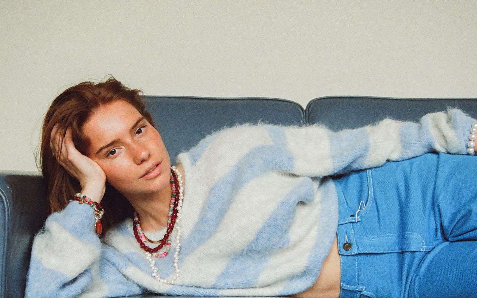 Lookbookbeeld van Bonnie: een vrouw met kralenkettingen in een blauw-witte trui, liggend op een bank
