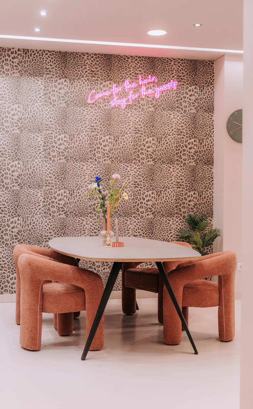 Roze stoelen rond een ronde tafel voor het panterbehang in de huiskamer van KUIF