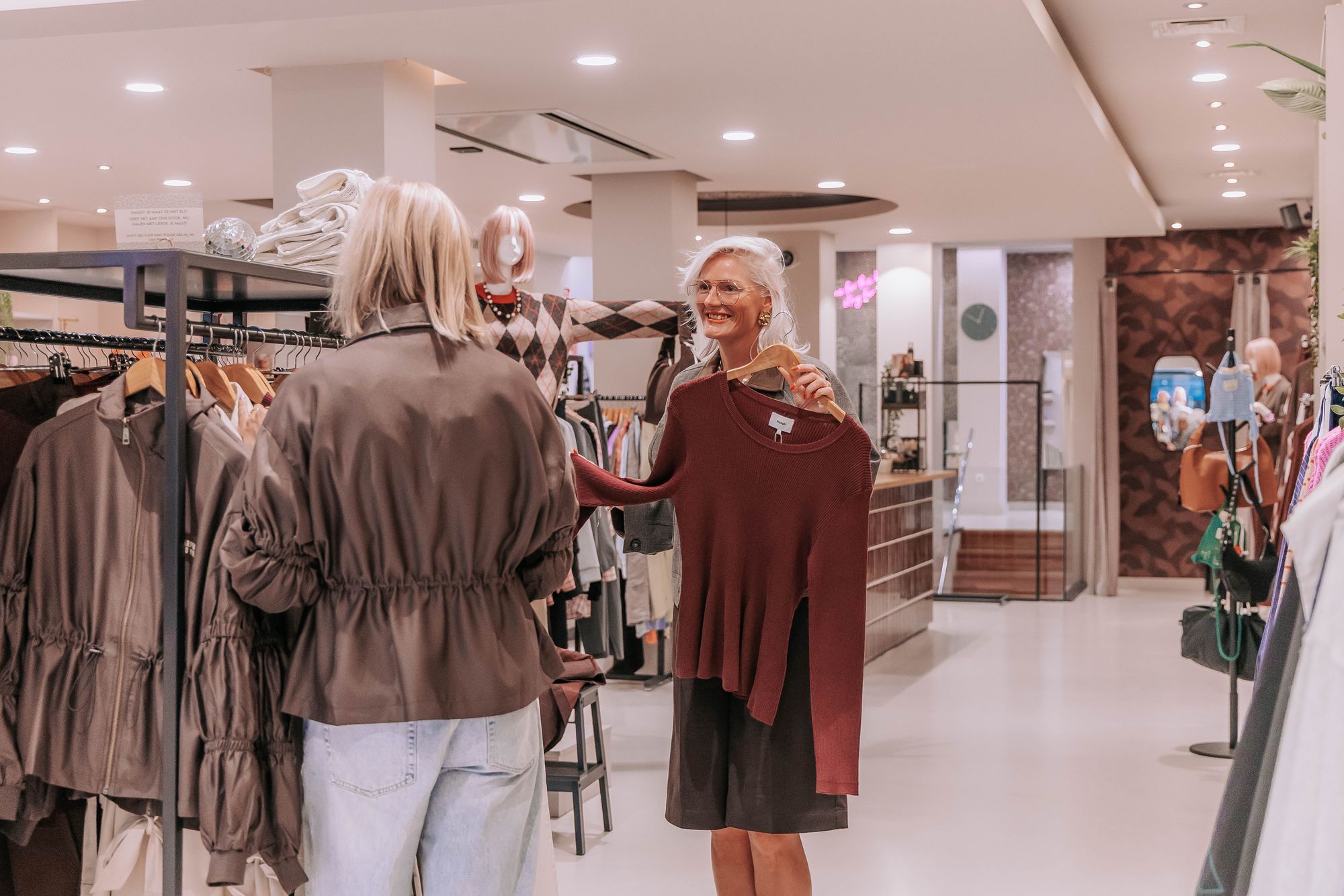 Ellie houdt in de winkel een rode trui omhoog voor een klant