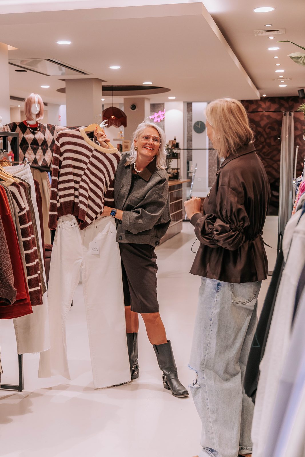 Ellie houdt in de winkel een gestreepte trui omhoog voor een klant in een bruine blouse